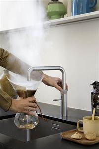 Heißes Wasser läuft aus dem Wasserhahn über den Kaffeefilter